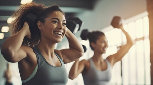 ClubOS | Two women smiling at gym lifting dumbbells